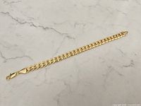 Full view of the chunky gold plated bracelet laid flat on a light marble surface.