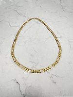 Full view of the gold plated Figaro style chain laid in oval shape