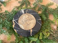 Top down view of paperweight showing bronze medallion with female figure on black marble base with natural veining.