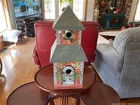 Front side of the hand painted two-tier wooden birdhouse showing artistic design and roofing