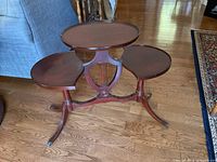 Full view of mahogany harp base side table showing three oval shelves and brass claw feet.