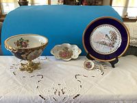 Set of five hand painted vintage Limoges porcelain decorative pieces displayed on a white lace tablecloth with blue backdrop