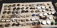 Top-down view of approx 36 cufflink pairs arranged on felt-lined tray