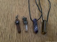 Four gemstone crystal pendants arranged on wood surface, showing different sizes and colors with two pendants on black cords.
