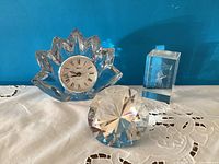 Wide view of Mikasa maple leaf shaped clock, Rosenthal diamond shaped paperweight, crystal etched cube paperweight on lace cloth background. Shows relative size and condition