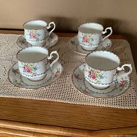 Four Royal Albert petit point cups and matching saucers displayed on a doily-covered wooden surface.