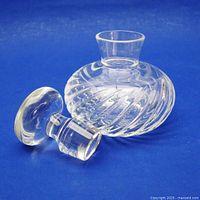 Crystal perfume bottle with swirl pattern on side lying on its side with stopper off, showing bottle shape and pattern details.