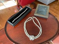 Photo showing sterling silver bracelet in box and double strand faux pearl necklace laid on wood table.