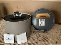 Swarovski crystal apple figurine inside a round grey box with foam insert, accompanied by two pamphlets and a separate round plaque with name plate.