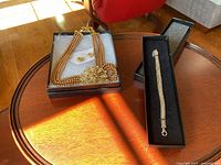 Full set displayed in box on round wooden table including necklace with floral centerpiece, matching earrings on card, and sterling silver bracelet in black box