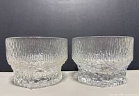 Front view of the two textured clear glass Iittala Alaska candleholders showing the bark-like pattern and heavy base.