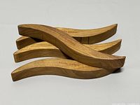 Four curved wooden wave trivets stacked, each stamped with Georg Jensen mark.