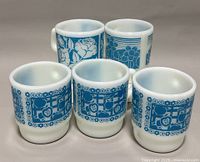 Photo showing front view of five vintage milk glass mugs arranged in rows, highlighting blue floral and fruit designs