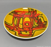 Front and angled view of the abstract decorated shallow bowl showing the red and black design on the yellow surface.