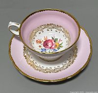 Photo showing the pink and gold teacup resting in the matching saucer, displaying the floral design inside the cup and on the saucer.