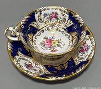 Front angled view of teacup sitting inside matching saucer showing floral and gold details on cobalt blue background.