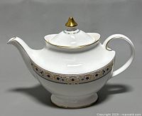 Front angle of bone china Royal Doulton Empress teapot showing gold finial, curved spout and patterned band
