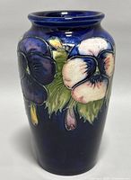 Front view of the dark blue Moorcroft vase showing floral relief design with light purple and cream flowers.