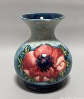 Front view of vintage Moorcroft vase with red poppy flower design against blue background.