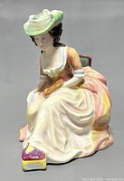 Front angle view of the Royal Doulton porcelain Kathleen figurine showing seated woman in pastel historical dress with palette and brush.