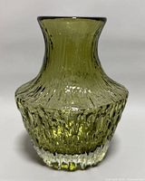 Front angle view of the vintage olive green Whitefriars glass vase with textured nailhead pattern and clear base, black-rimmed flared mouth.