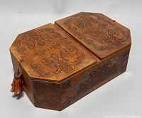 Closed view of the wood jewelry box showing detailed hand-carved patterns on the lid and sides with a leather tassel on the front.