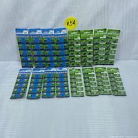 Photo showing full set of 48 button cell batteries separated in two groupings of 24 cards each, arranged on white surface with yellow lot tag #54 visible.