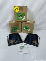 Three boxed units of solar motion sensor security lights with two units unpacked showing solar panels and installation accessories.