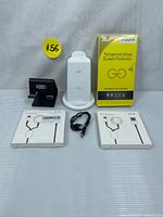 All items in the bundle laid out on a white surface: black phone stand, white wireless charging station, Samsung tempered glass screen protector box, two Lightning cables in packaging.