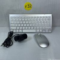 Front view of slim silver wireless keyboard, silver wireless mouse, and black USB webcam with USB cable.