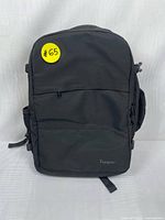 Front view of the black Taygeer laptop bag showing the compact rectangular design with a small front pocket and yellow sticker labeled #65.