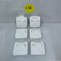 Six pairs of Apple wired earphones Class A copy in white cardboard packaging arranged in two rows, with a yellow sticker #36 behind.