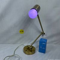 Wall-mounted brass lamp with adjustable arm illuminated with purple glow from smart LED bulb; clear power cord visible; bulb box shown.