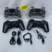 Top view of four gaming controllers and four charging cables displayed on a white surface, showing two clear case and two black case controllers.