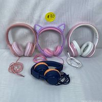 Four wired headsets displayed side by side showing various styles and colors including pink, white, purple cat ears, navy blue and orange.