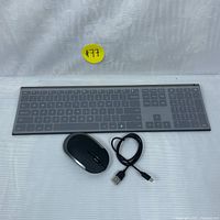 Keyboard with silicone grey cover, wireless mouse, and charging cable laid flat on a white cloth background.