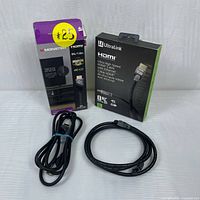 Two HDMI cables visible with their original packaging. Monster cable packaged in purple and black, UltraLink cable packaged in black and green box. Cables coiled and placed in front of their boxes on a white background.