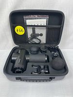 Front view of massage gun and six attachments placed inside a gray hard-shell carrying case with mesh pocket holding USB cable and user manual.