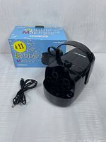 Front angle of black QB-806 bubble machine with multiple circular bubble outlets, power cord coiled next to unit, and original blue box with colorful bubble graphics behind.