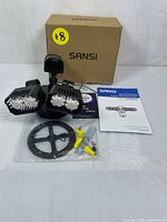 Photo of Sansi motion-activated ceramic LED security light with box, mounting bracket, screws, wire connectors, and instruction manuals laid out on surface.