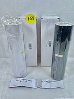 Photo showing two self-adhesive vinyl rolls in original packaging, one white and one black, with instruction sheets in front.