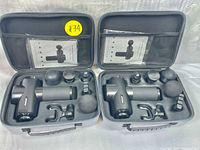 Photo showing both fascial massager sets with devices, multiple attachments, and user manuals neatly arranged inside hard carrying cases.