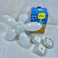 Photo of LED deformed egg lamp showing five white petal-shaped adjustable panels and original packaging box, along with three small square motion sensor lights.
