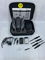 Zuhafa FPV drone and controller inside the carrying case with manuals visible, plus spare batteries, propellers, screwdriver, and USB cable laid out beneath.