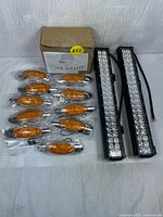 Ten amber oval side marker lights with chrome bases individually packaged, two LED light bars with black metal housing and wiring, cardboard box labeled 'CAPD LIGHTS'.