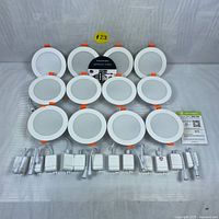 12 round 4-inch LED recessed lights with white trim and orange clips, laid out with 12 white junction boxes and connectors on striped fabric background.