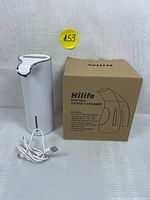 White automatic soap dispenser and its USB charging cable with HiLife garment steamer box visible behind the soap dispenser.