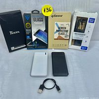 Photo of two Maxlife 10000mAh power banks (white and black), two screen protectors in packaging (one for Galaxy S21 and one for iPhone 6-8 Plus), Galaxy S21 battery case in packaging, and a USB charging cable.