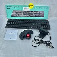 Wireless keyboard, ergonomic trackball mouse, USB webcam, user manual, and keyboard box arranged on surface showing all included items.
