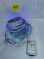 Coiled RGB WS2812B LED strip light illuminated with blue light, accompanied by remote control and power adapter on a striped fabric surface.